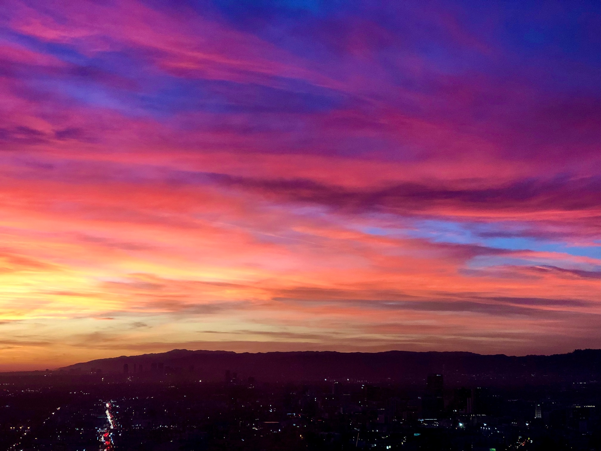 Sunset cityscape over Los Angeles with glowing skyline and mountain silhouettes